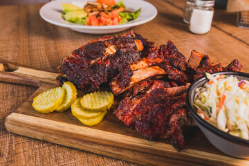 Baby back ribs served with pickles on a wooden board at a well lit modern food restaurant 