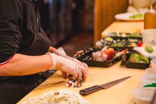A sushi chef wearing clear protective gloves while placing sushi in to go containers at a Japanese hibachi restaurant 