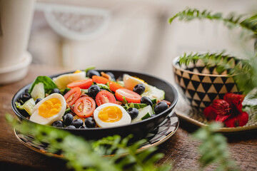 A colorful breakfast and brunch salad with lettuce eggs, tomatoes and blueberries in a bright modern restaurant with plants 