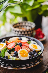 A colorful breakfast and brunch salad with lettuce eggs, tomatoes and blueberries in a bright modern restaurant with plants 