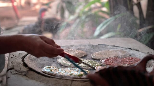 Hands of mature Mexican women preparing Mexican food on a clay comal, smoke rising from the hot comal