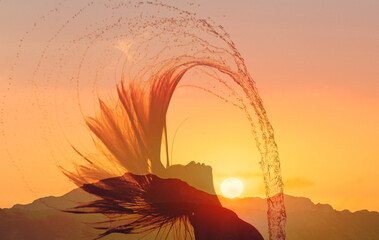 Young woman whips her hair back and splashes water over the sunset