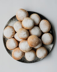 Powdered sugar donut black plate overhead minimal white background sweet dessert pastry round pile. Powdered sugar donut black plate, overhead view minimal white background, sweet dessert pastry