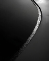 Curved basalt shoreline monochrome water edge minimal seascape smooth surface serene mood high contrast abstract curve rocky barrier coastal detail tranquil scene evoking calm and quiet