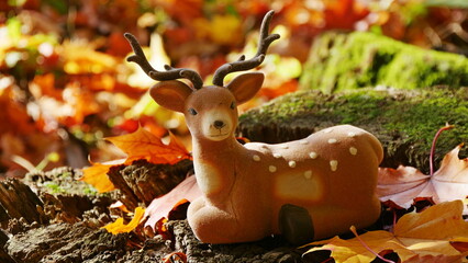 A toy deer among bright fallen leaves in the wood on an autumn day.