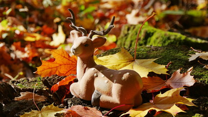A toy deer among bright fallen leaves in the wood on an autumn day.