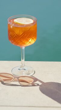 Orange, cocktail and sunglasses with water by pool for hospitality at summer getaway or resort. Empty, drink or cool mocktail with lemon or shades for weekend vacation, party or vitamin C by poolside