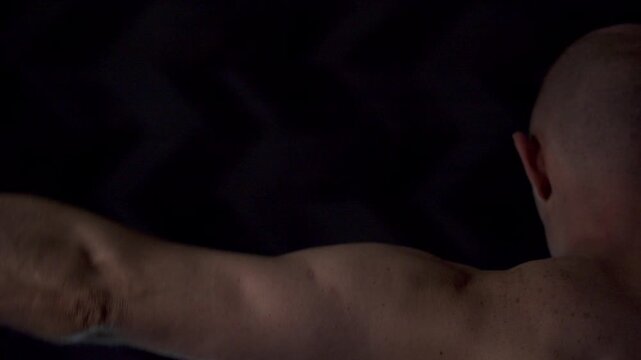 Close-up portrait of an athletic man against a dark background. View from the back, the guy raises his arms up, then lowers them, tensing his muscles, showing his power and strength.