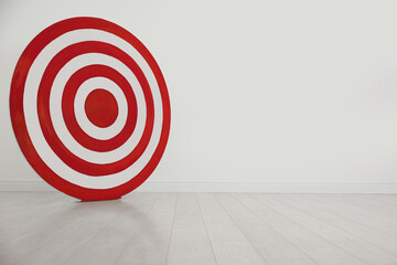 Round shooting target on floor near white wall, space for text