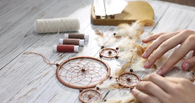 Woman making beautiful dream catcher at light wooden table, closeup