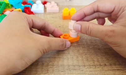 Fototapeta premium an asian woman is playing with lego forming the legs to form a giraffe with a brown background