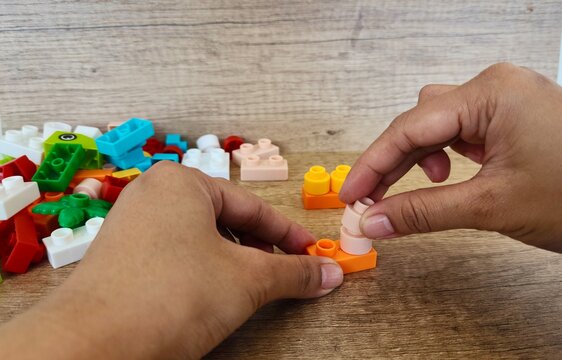 an asian woman is playing with lego forming the legs to form a giraffe with a brown background