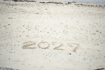 The number 2027 written on sandy beach under bright sunlight, symbolizing new beginnings, travel, and the coming future
