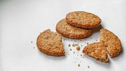A close-up shot of crispy oat cookies with broken pieces and crumbs scattered on a clean white surface.