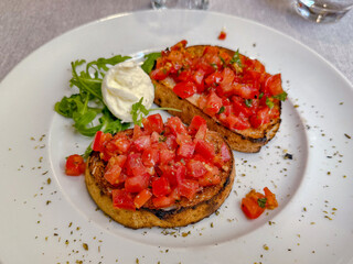 Bruschetta topped with tomato, garlic and basil on white plate.