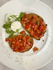 Bruschetta topped with tomato, garlic and basil on white plate.