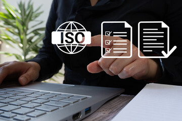 A woman working at a computer pointing at an ISO certification icon, with documents being reviewed