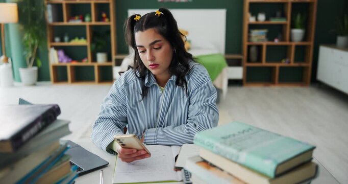 Homework, student and girl with smartphone, bored and exhausted with burnout, distracted and fatigue. Apartment, person or woman with books, tired or cellphone with education, study or procrastinate