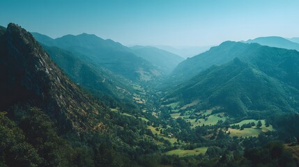 Fototapeta premium Lush green valley nestled between misty mountain ranges under a clear sky.
