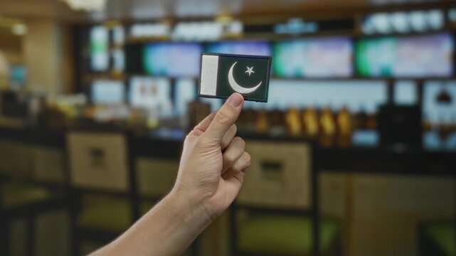 Man holding embroidered pakistan flag patch indoors in a coffee restaurant with a blurred background.