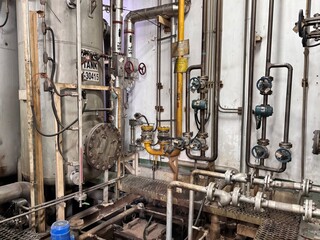 Intricate network of aging industrial piping and valves inside a factory or plant facility,...