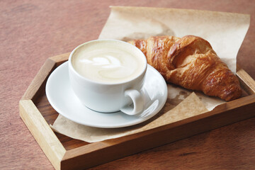 Warm coffee and fresh croissant on a wooden tray
