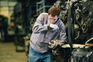 White man technician checking used car damaged engine block at scrap yard warehouse recycle area...