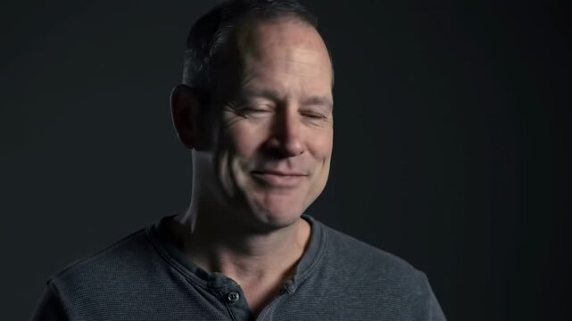 Portrait shot featuring a mature, smiling man in a Henley shirt against a dark background