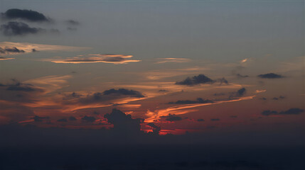 Obraz premium Dramatic sunset sky filled with orange and red hues peeking through dark, scattered clouds.
