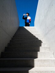 Man drinking water from bottle on top of concrete stairs against a clear blue sky