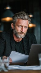 Mature businessman or investor analyzing data on laptop with paperwork at desk