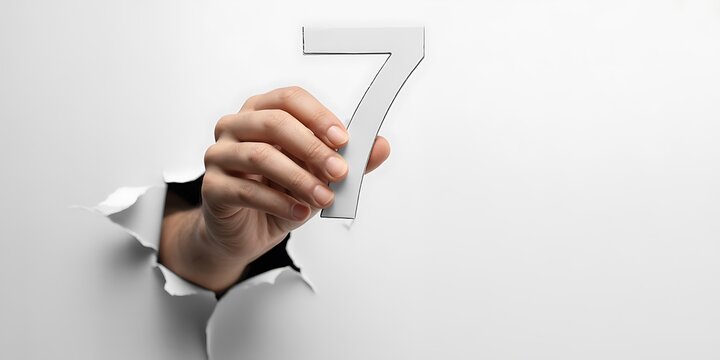 Realistic Hand Holding Number 7 Through Torn Paper on White Background