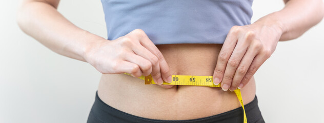 Young slim woman measuring her waist by measure tape after a diet