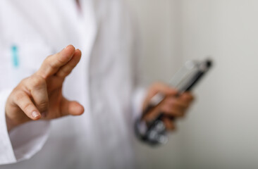 Close-up of a doctor's hand reaching out holding stethoscope against a white background. Concept of...