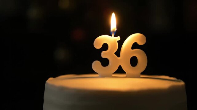 A birthday cake in the dark with a lit number "36" candle on top.