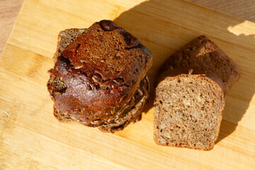 sliced bread piled up in a pyramid next to 2 pieces of bread with crust and seeds on it on a wooden surface, viewed from above