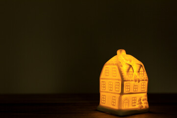 A glowing ceramic house on a wooden surface, bathed in a warm, inviting light. The cozy ambiance...