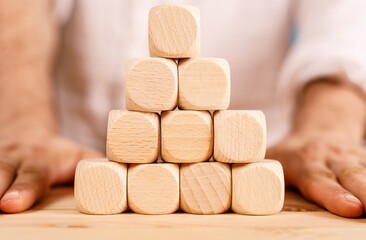 Close-up of hands surrounding a pyramid of wooden blocks on a table. Concepts of building, teamwork, or growth.