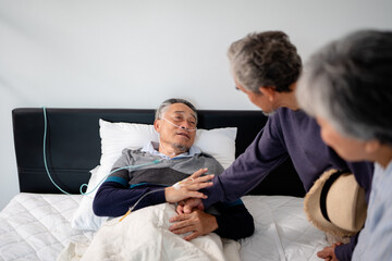scene of bedridden patient, elderly hopeless senior man lying on bed with oxygen mask by doctor. home caregiver nurse visit retirement patient for health check up recovery process medical service