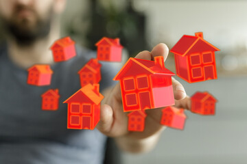 Hand presenting floating red house models, symbolizing real estate, property market, investment, and home ownership.