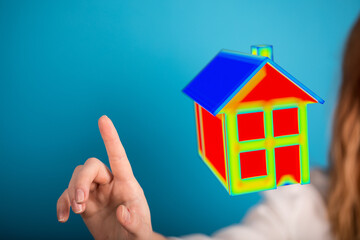 A woman's finger interacts with a miniature house against a blue backdrop. Perfect for representing concepts of real estate, home ownership and