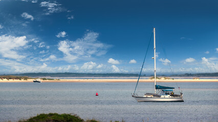 A sailboat anchored off Cape Lookout, North Carolina, under clear blue skies and bright clouds...