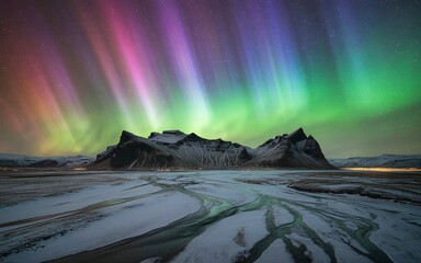 Naklejka premium Vibrant aurora borealis illuminates a majestic snowy mountain landscape at night.