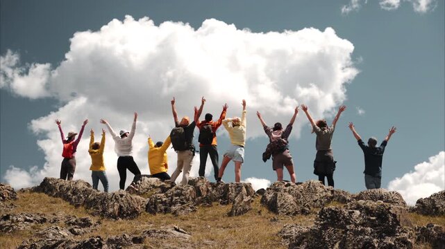 Big and diverse group of young hikers or tourists are standing at mountain top with open arms in winner poses