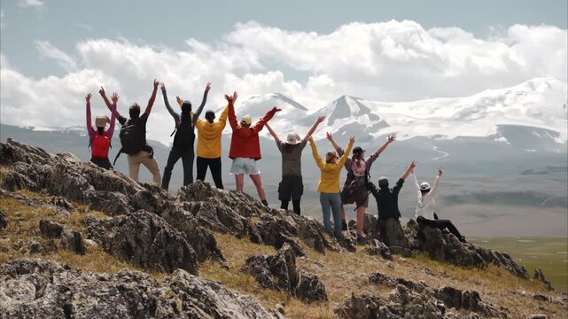 Big group of young diverse hikers are standing against snow capped mountain at winner poses with open arms and enjoys great view