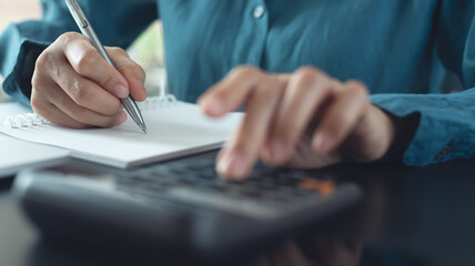 Close up woman hand using calculator to calculate home finance and writing note, accounting on...