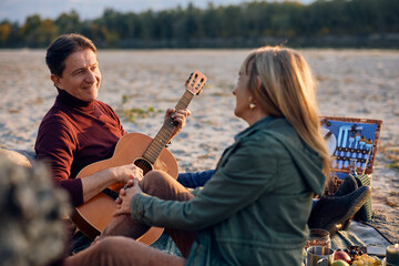 Romantic man playing acoustic guitar to his wife on autumn picnic in nature.