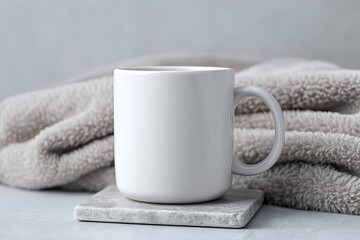 Plain white ceramic mug on a marble coaster with a soft beige blanket behind it