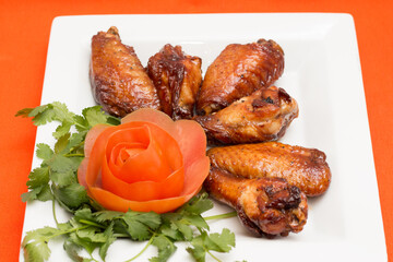 Grilled chicken wing with cucumber and carrot garnish on white plate