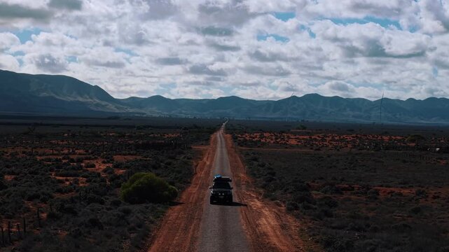 Aerial drone footage of a 4WD driving along a desolate outback road in South Australia, passing towering wind farms, showcasing rugged terrain, remote landscapes, and renewable energy in the outback.